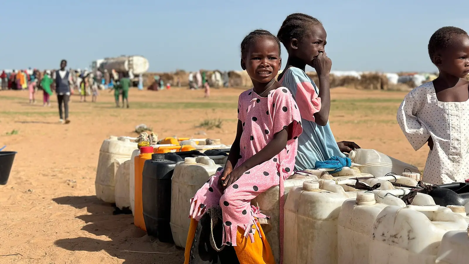 A girl waiting beside water containers in a displacement camp in Sudan
