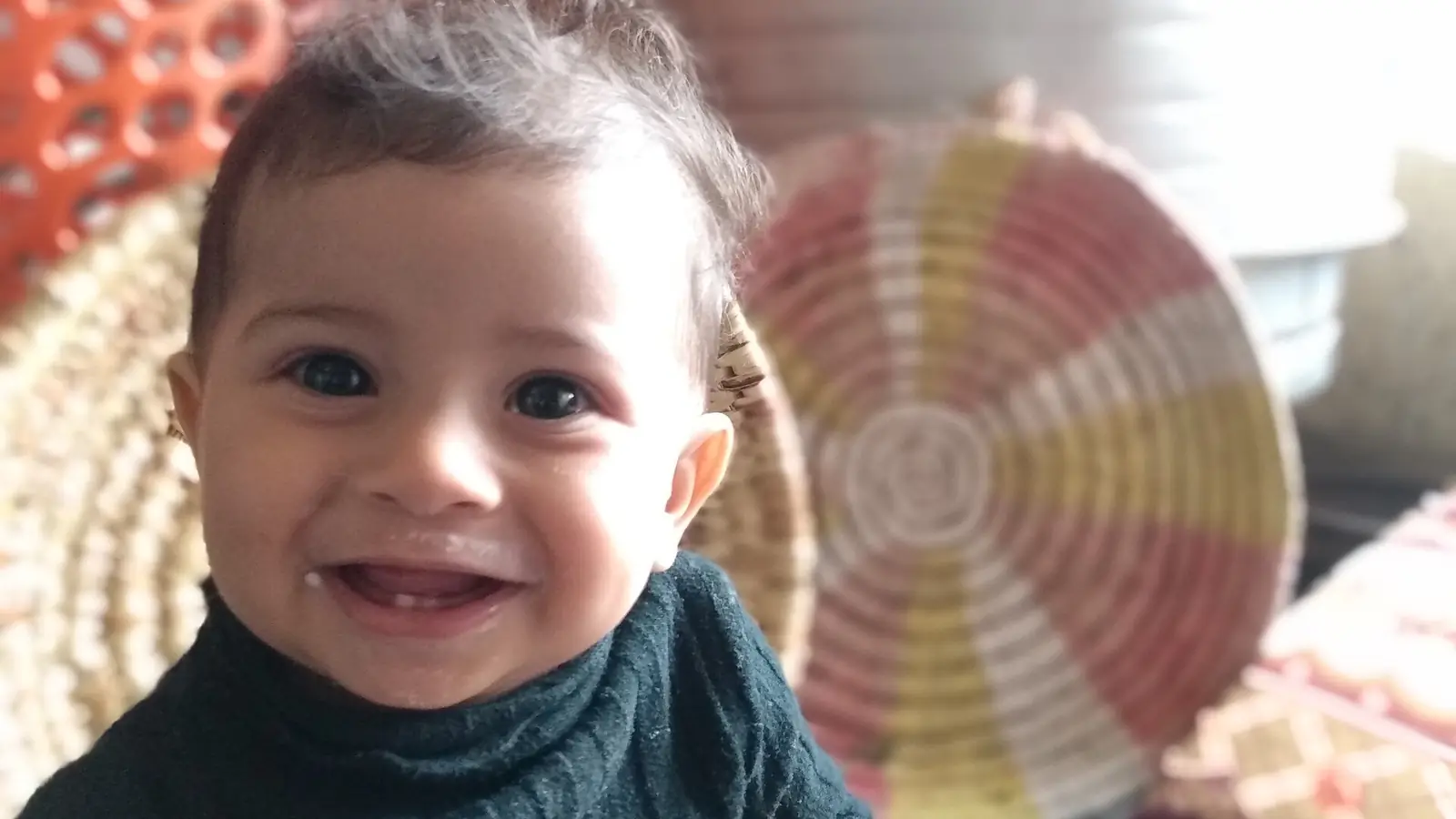A smiling Yemeni toddler in front of traditional handwoven baskets